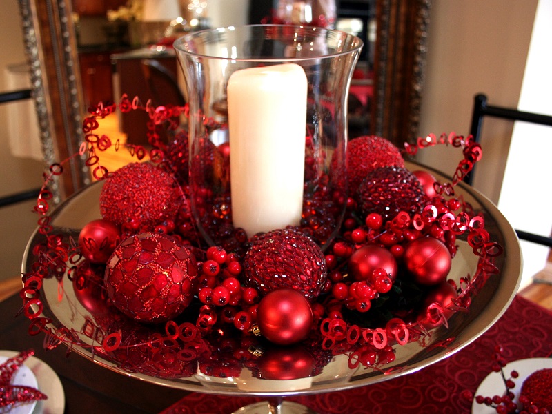 Candle display with glass votive, red ornaments, and christmas decor on a tray.